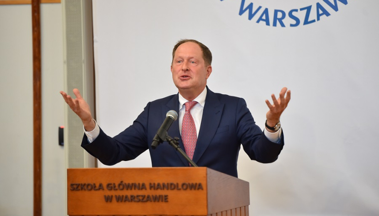 mężczyzna z rozłożonymi rękami przemawia zza mównicy