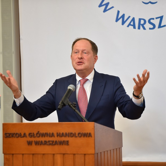 mężczyzna z rozłożonymi rękami przemawia zza mównicy